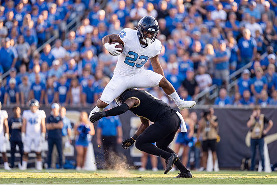 Football player number 23 hurdling over a defender. 