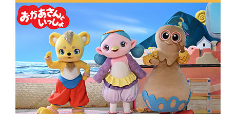Okaasan to Issho show banner: costumed characters Luchita, Mimomo, and Yakor standing outdoors in front of a colorful backdrop.